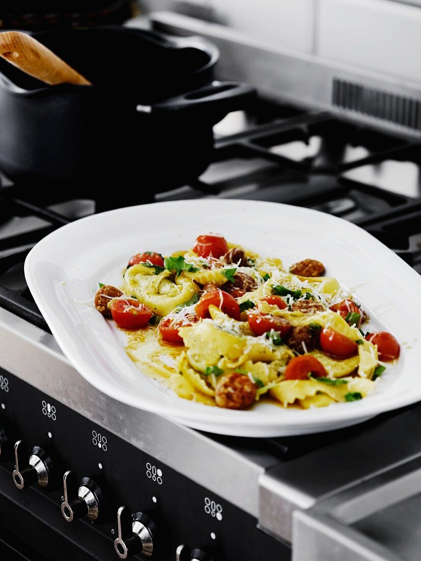 Tortellini with tomatoes and mushrooms on a serving platter on a stove in a kitchen