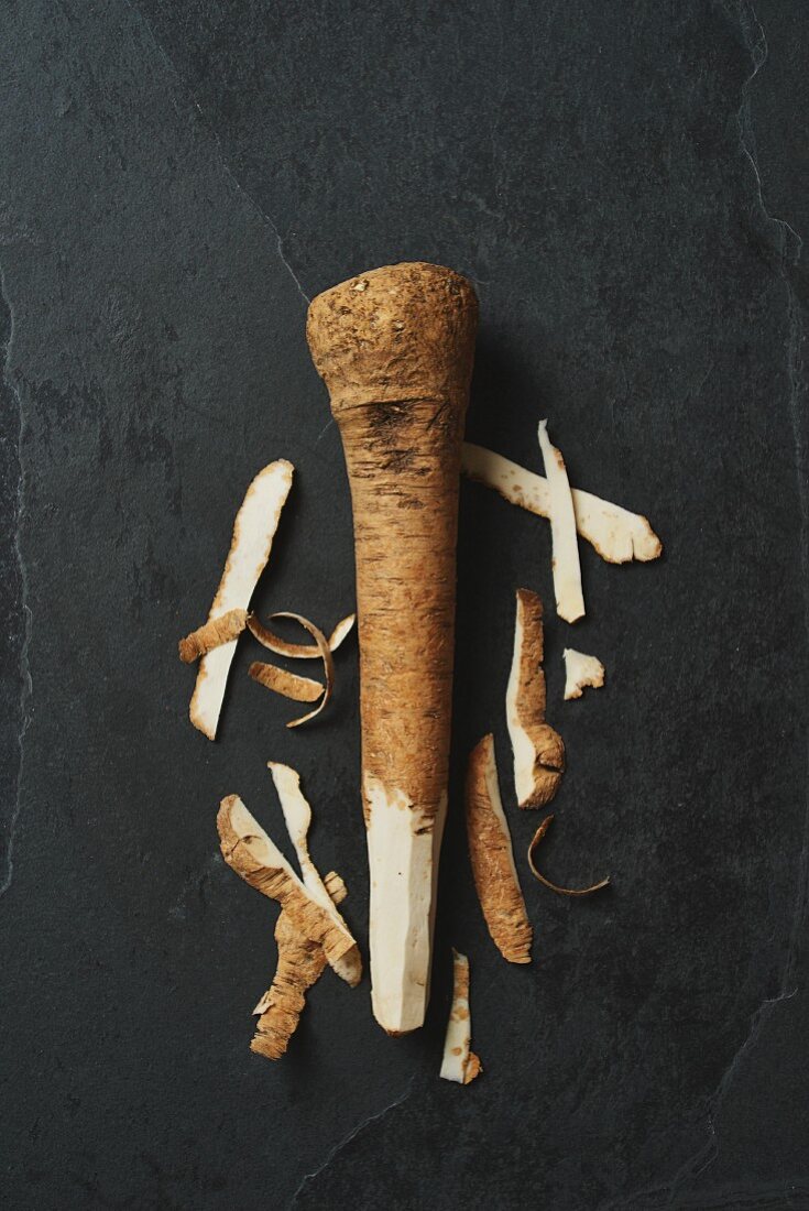 A horseradish root on a grey surface, partially peeled