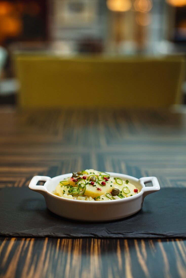 Kartoffelsalat mit Pfefferbeeren & Kapern in Schale auf Restauranttisch