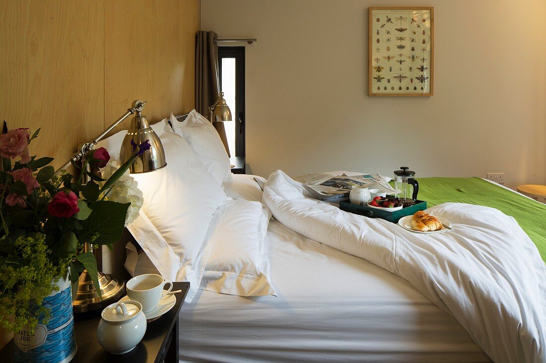 Tray on double bed with white bedlinen and retro table lamp on bedside table in modern bedroom