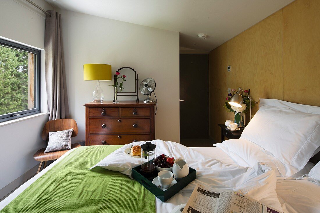 Breakfast tray on double bed and table lamp on traditional chest of drawers