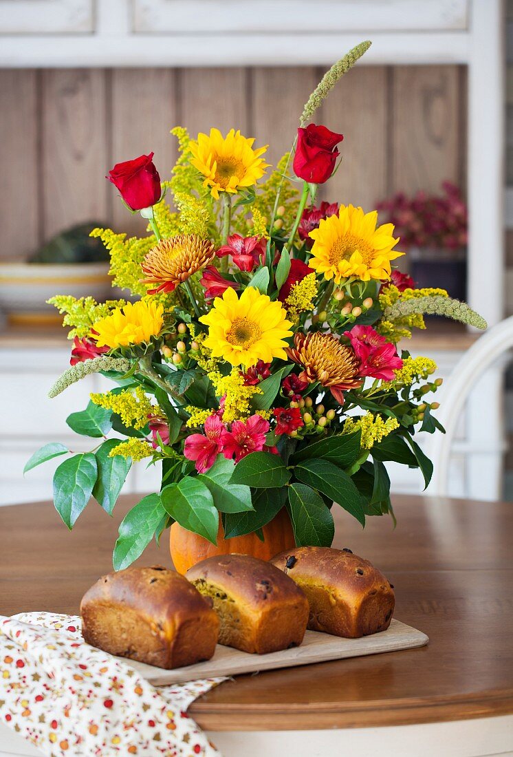 Three loaves of pumpkin bread with raisins, dried cherries and pumpkin seeds in front of a bouquet of flowers