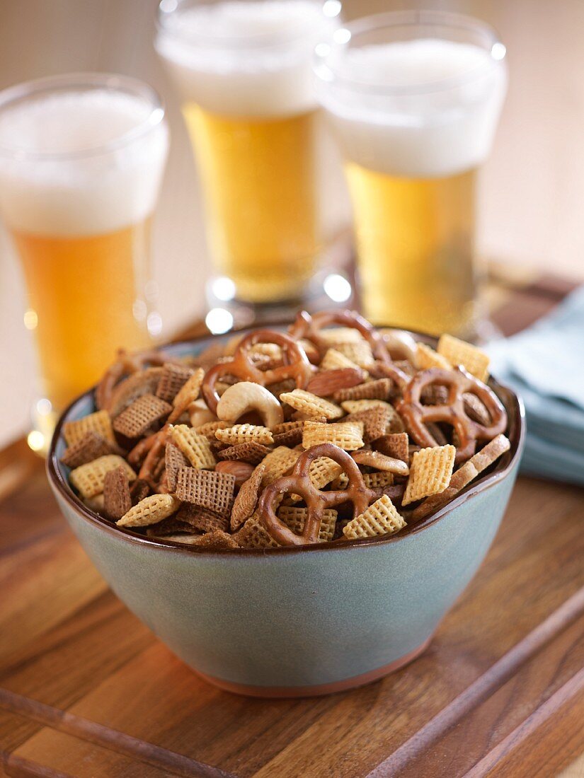 A bowl of snacks with glasses of beer in the background