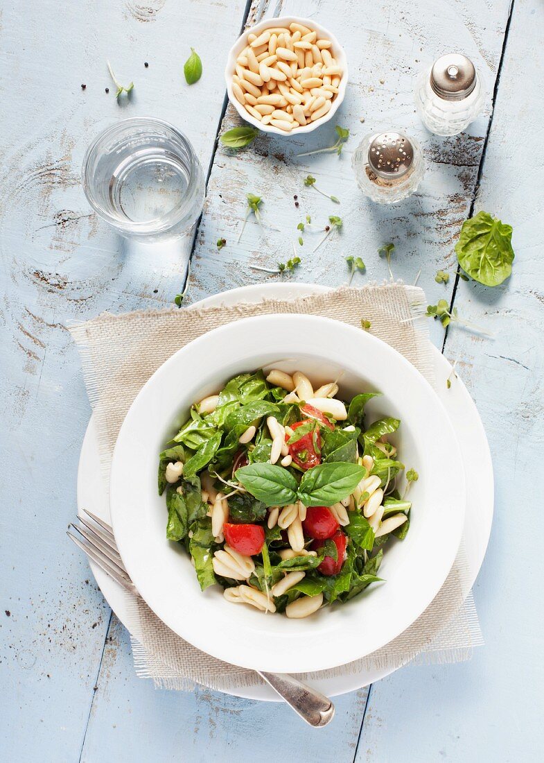 A bowl of pasta and spinach salad with tomatoes and pine nuts