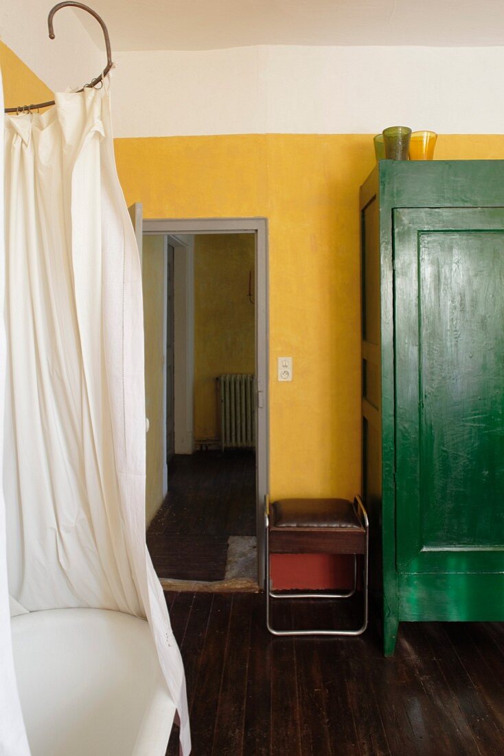 Vintage-style bathtub, shower curtain and green-painted cupboard against yellow wall