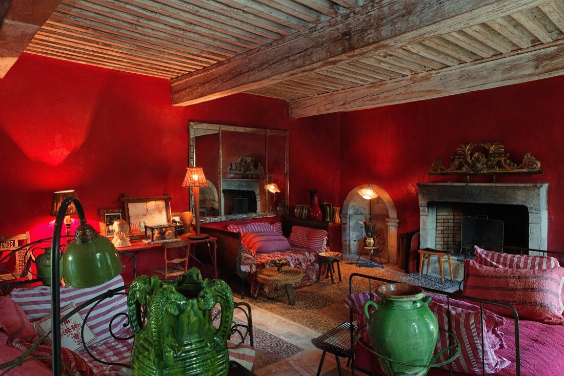 Stimmungsvoller Wohnbereich mit leuchtenden Tischlampen vor roten Wänden, Vintage Schlittenbetten und offenem Kamin