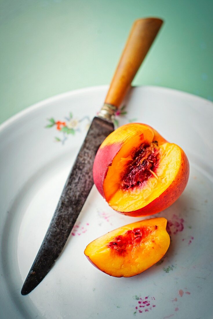 A nectarine, sliced, on a plate with a knife