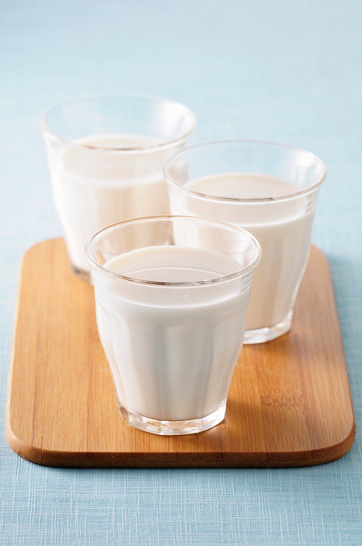 Three glasses of milk on a chopping board