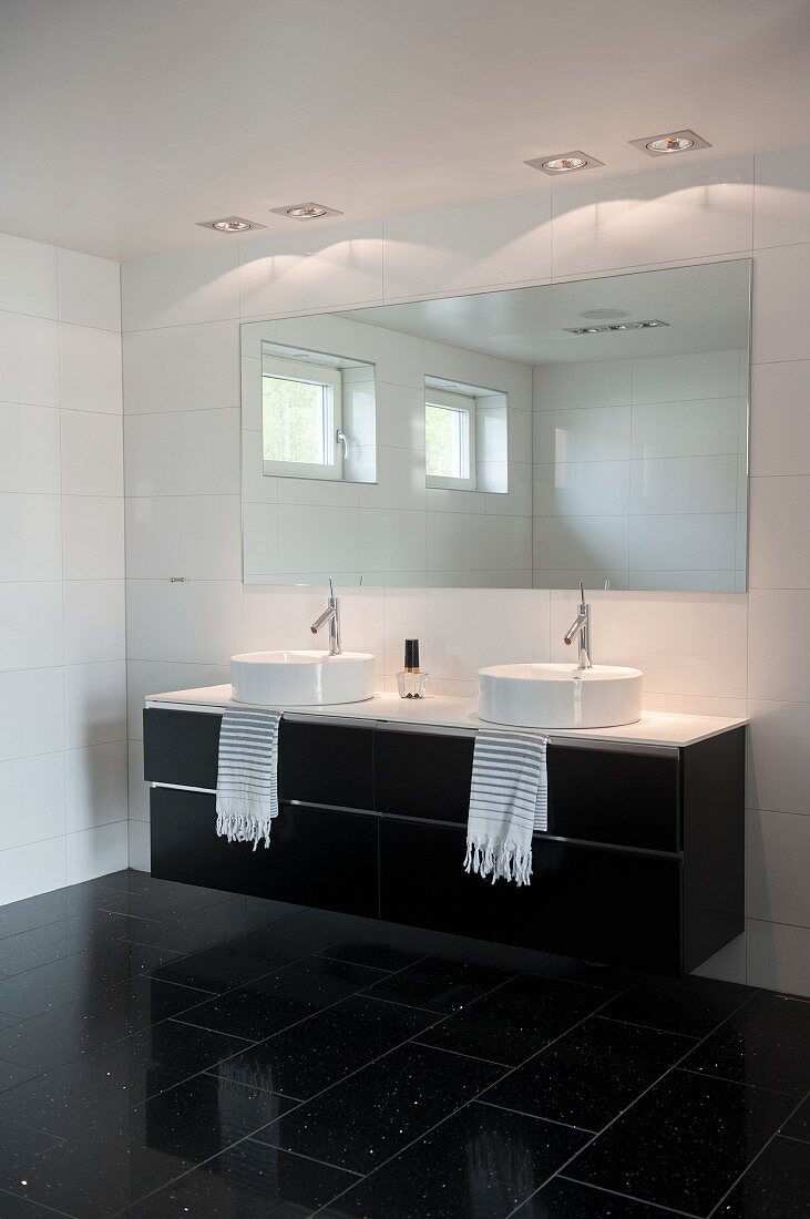 Washstand with twin countertop sinks below mirror in black and white designer bathroom