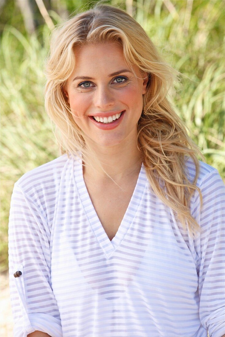 A young blonde woman on a beach wearing a transparent striped top