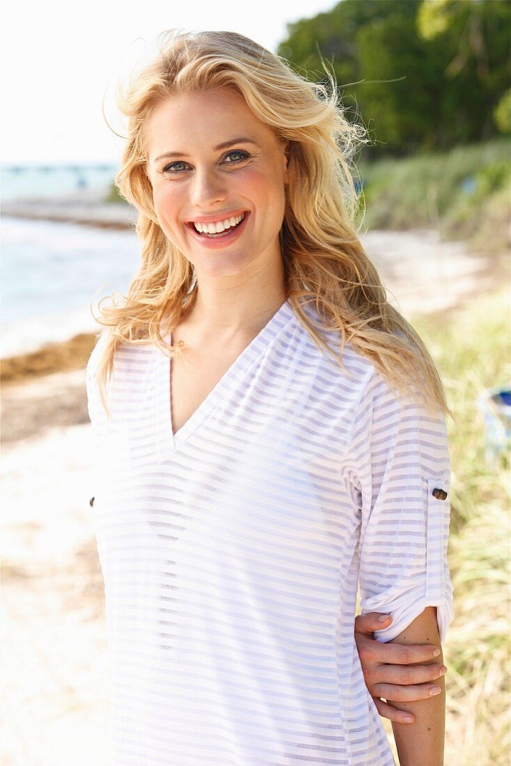 A young blonde woman on a beach wearing a transparent striped top