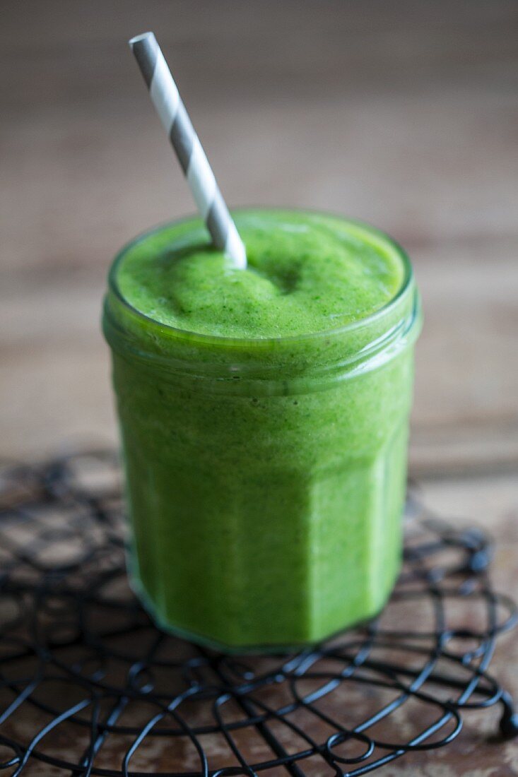 A green smoothie in a screw-top jar with a straw