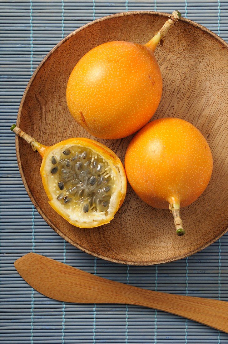 Yellow passion fruits, whole and halved, on a wooden plate