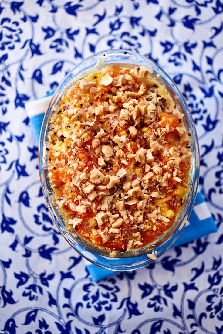 Tomato gratin with chopped nuts in a glass baking dish