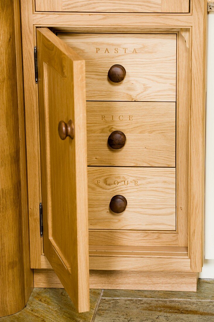 Oak base unit with open door and drawers labelled with names of various dry goods