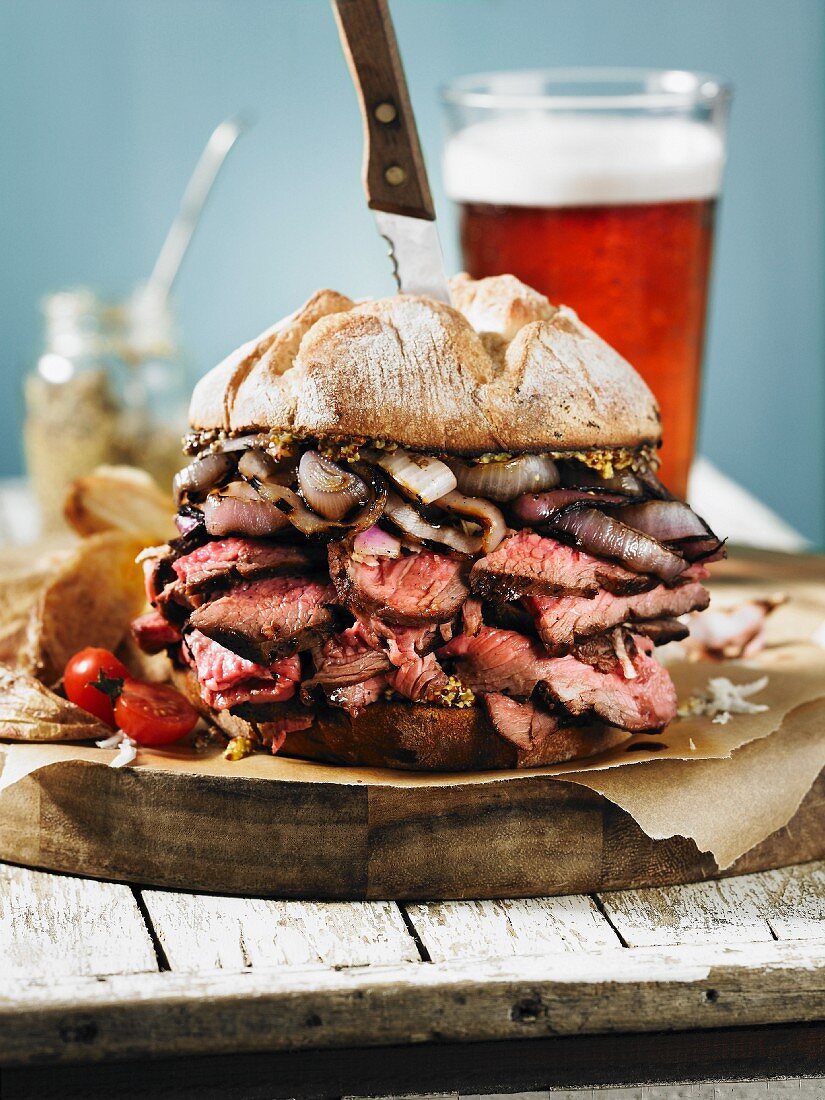 A giant steak sandwich on a wooden board with a beer