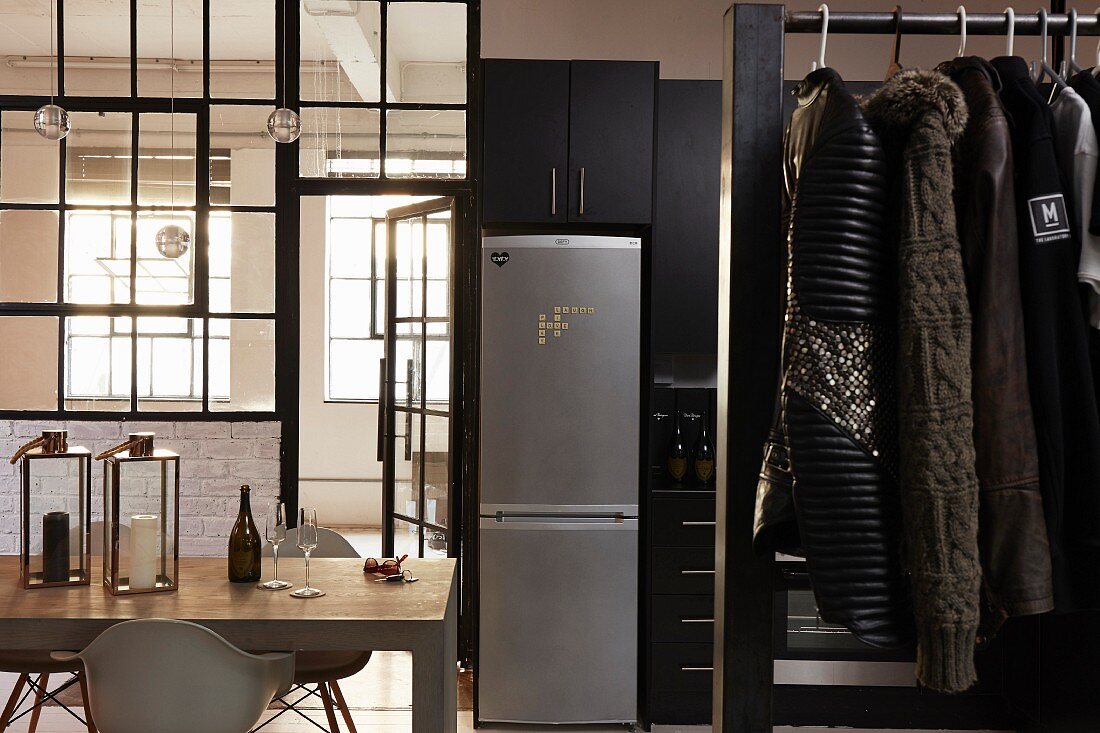 Classic chairs around dining table, glass partition and men's coats hanging from clothe rail in foreground