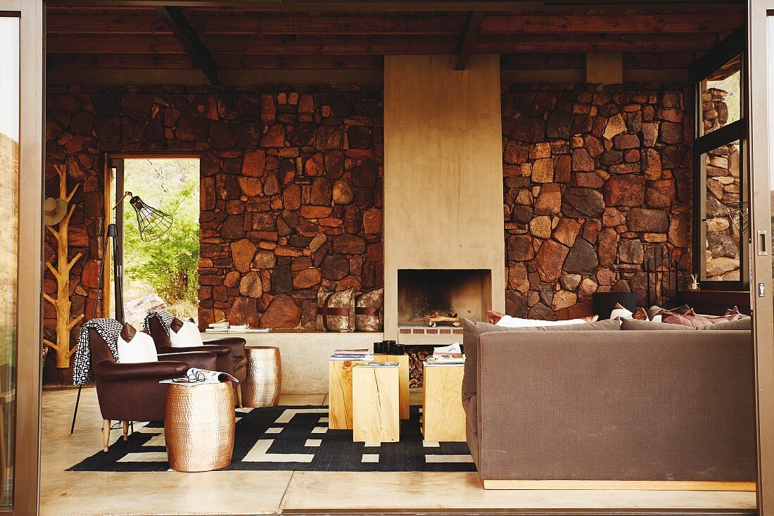 Brown chairs and side tables in Colonial-style interior with open fireplace in stone wall and open terrace doors