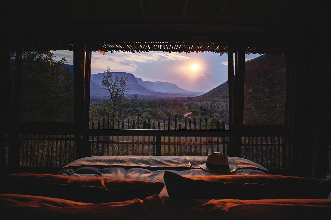 Romantischer Blick vom Bett durch Panoramafront auf Sonnenuntergang in Safari-Landschaft