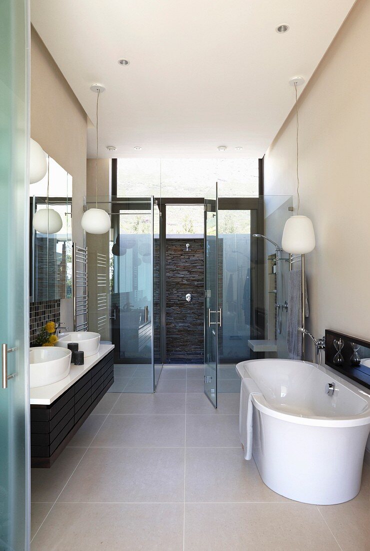 Modernes Bad mit freistehender Badewanne auf grossformatigem Fliesenboden vor verglastem Duschbereich