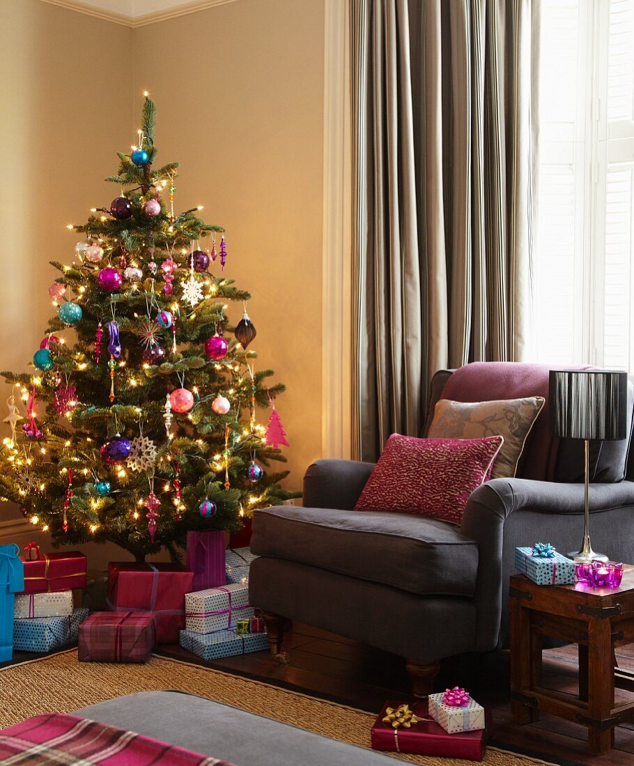 Geschmückter Weihnachtsbaum und Geschenke neben braunem Polstersessel in Wohnzimmerecke