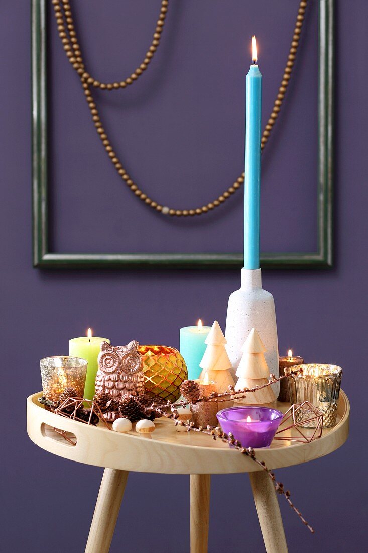 Colourful collection of candles on tray table in front of purple wall