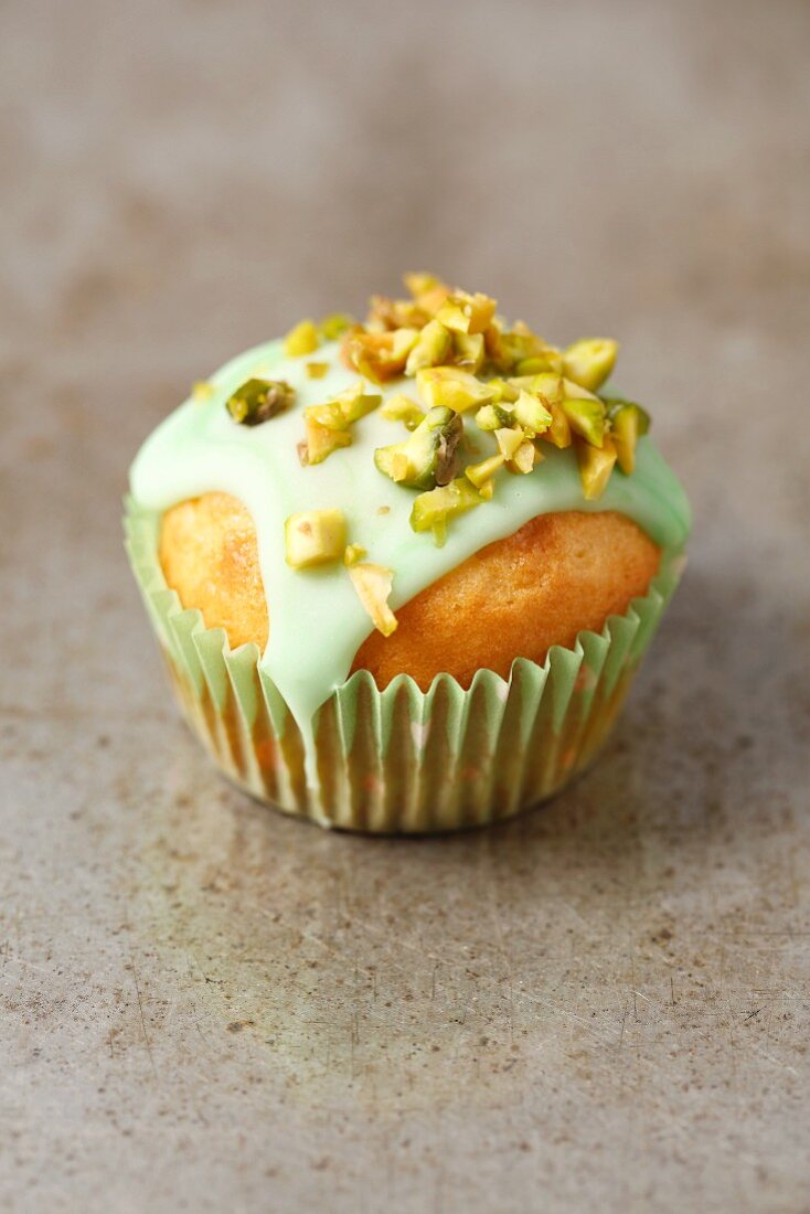 A pistachio cupcake with green icing and chopped pistachio nuts