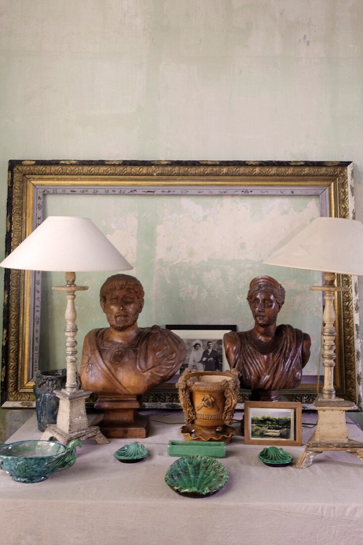 Arrangement of ceramic objects, antique table lamps with white lampshades, wooden busts and picture frames