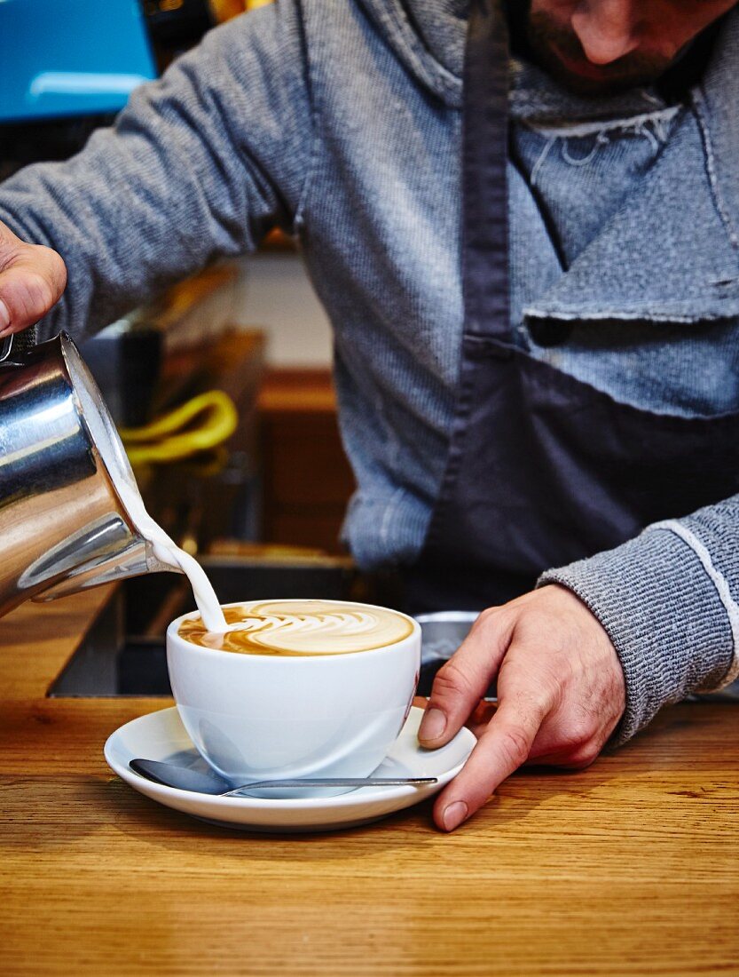 A barista pouring milk foam into a coffee cup