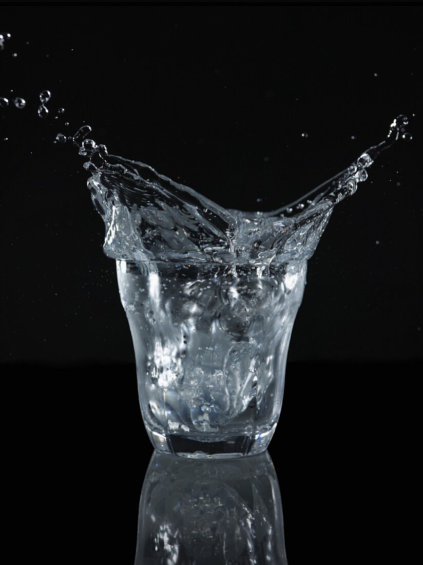 Wasser spritzt aus Glas vor schwarzem Hintergrund