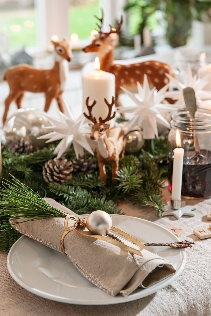 Linen napkin decorated with sprig of pine and silver bauble on plate on festive dining table