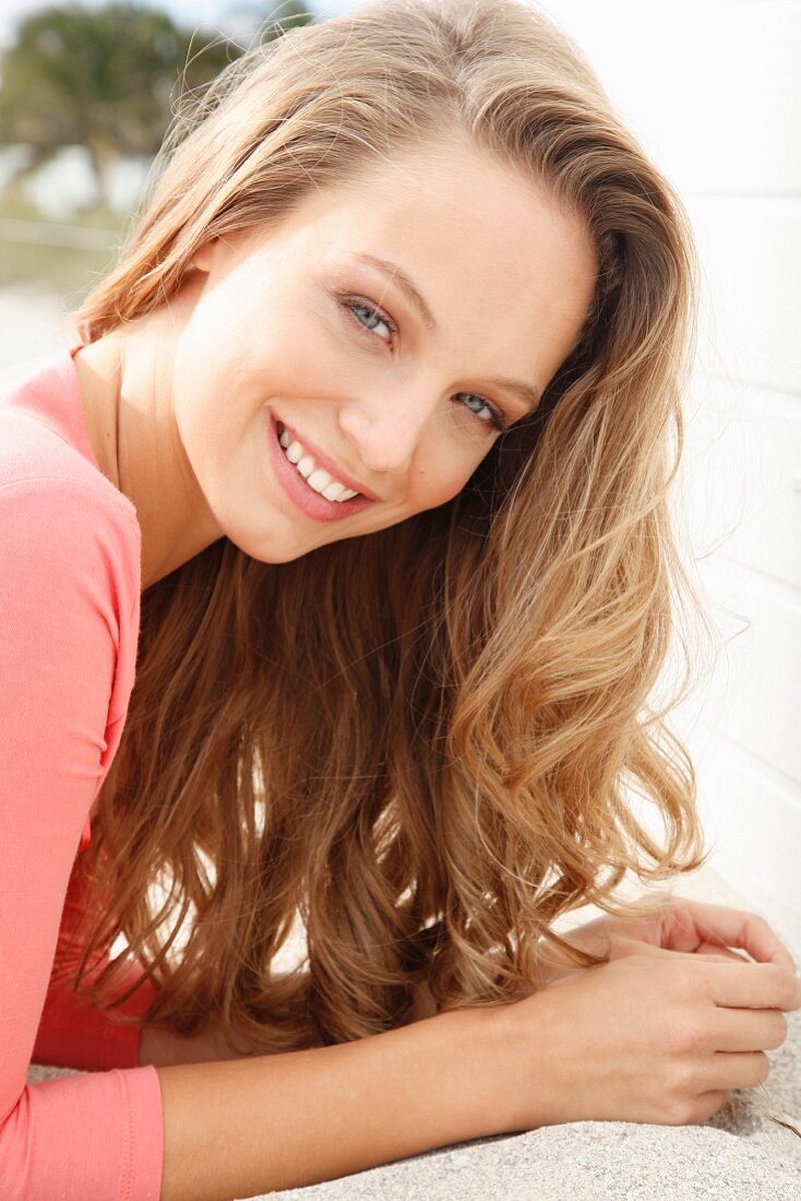 A young blonde woman lying on a beach wearing a salmon-coloured top