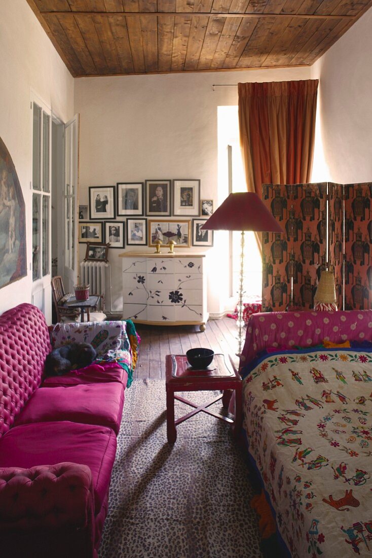 Pinkfarbenes Sofa gegenüber Tagesbett mit folkloristischer Decke in eklektischem Ambiente