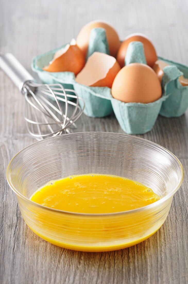 Egg yolks in a bowl, eggs in an egg box and a whisk