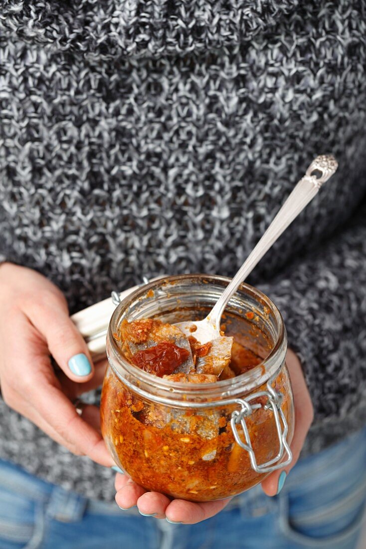 A woman holding a jar of herring in dried tomato pesto