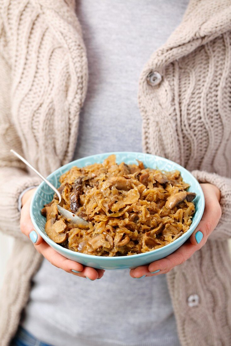 A woman holding a bowl of braised sauerkraut with mushrooms