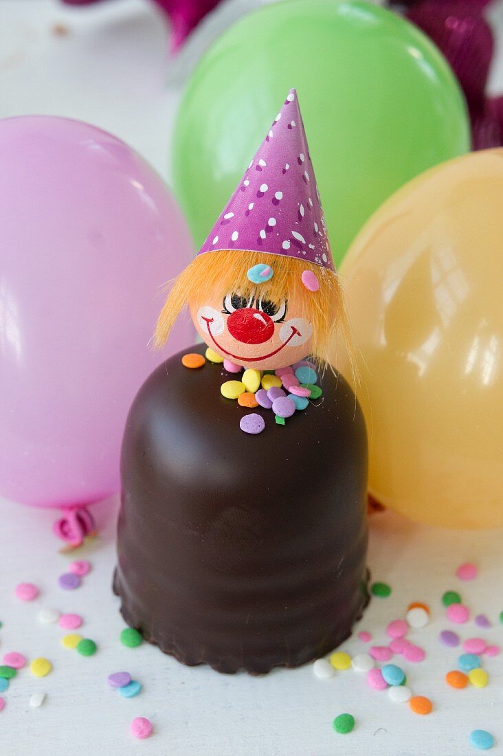 A chocolate candy with a clown face, balloons and sugar confetti