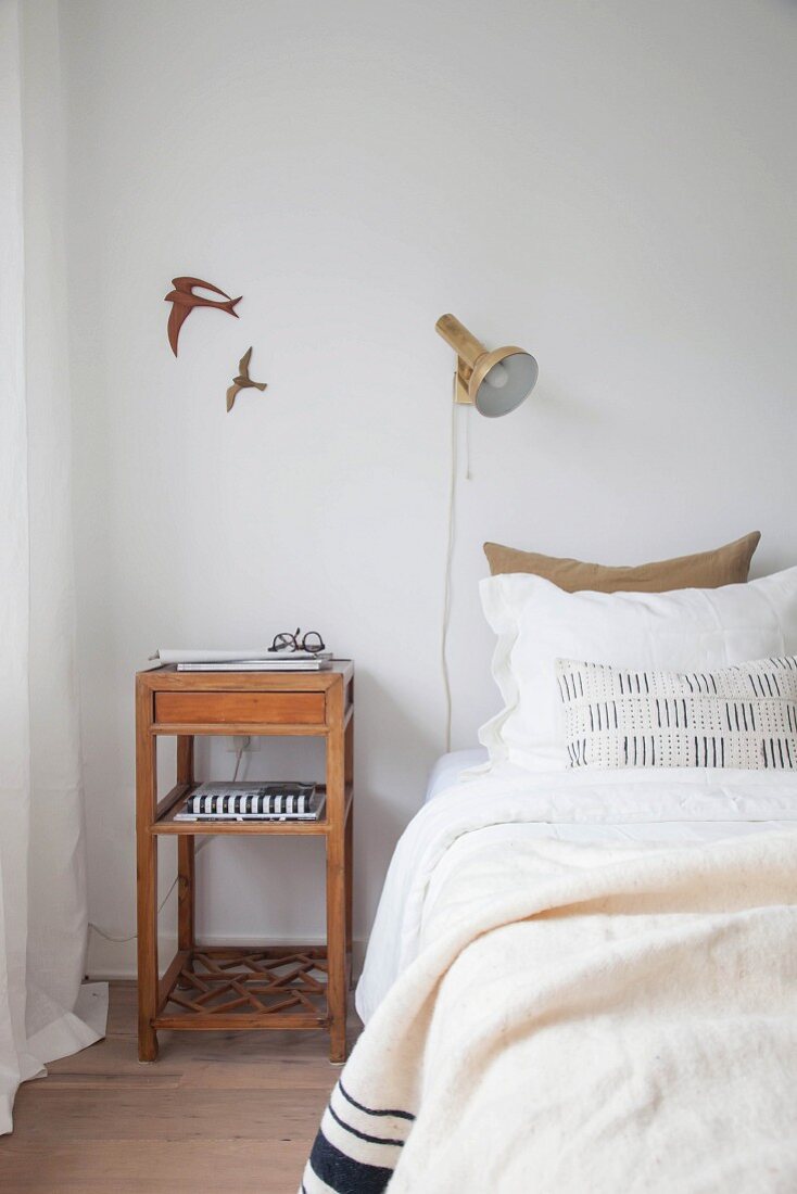 Simple wooden bedside table next to bed below bird motifs on wall and wall-mounted lamp