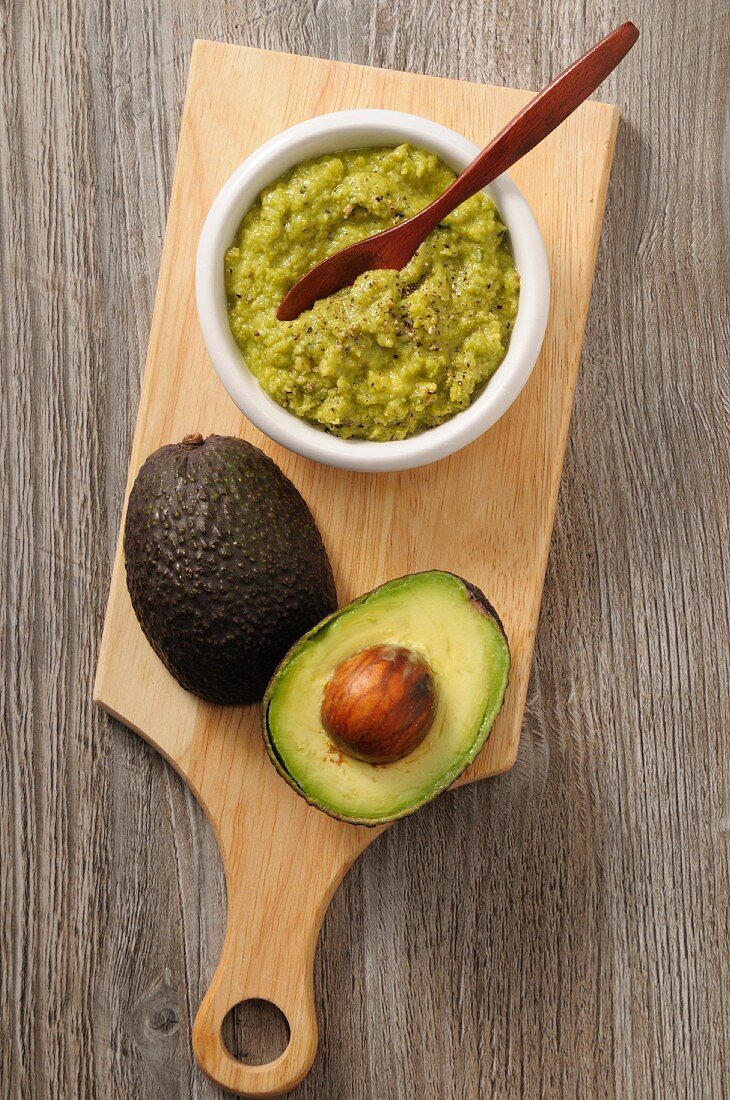 Guacamole and a fresh avocado on a chopping board