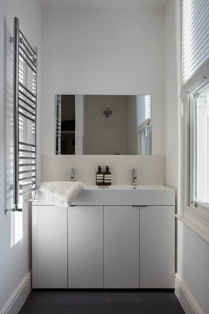 Doppelwaschtisch mit weißem Unterschrank und glänzendem Handtuchtrockner in schmalem Bad mit Fenster