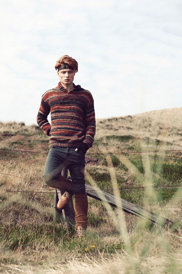 A young red-haired man wearing jeans and a stripy, knitted jumper