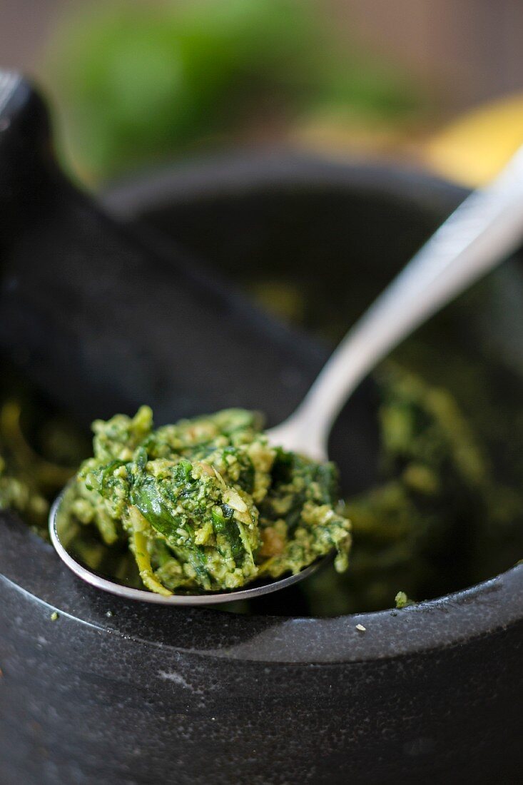 Basil pesto with lemon and walnuts on a spoon and in a mortar