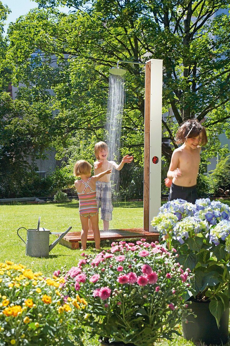 Kinder spielen im Garten unter einer Außendusche