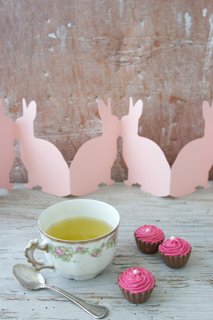 Spring herb tea in vintage cup, chocolates and paper Easter bunnies