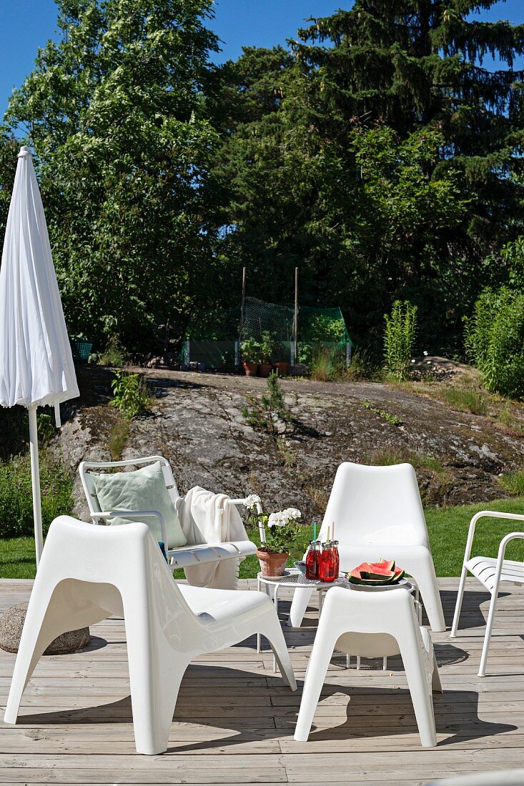 White plastic outdoor easy chairs on sunny wooden deck in garden with boulders in background