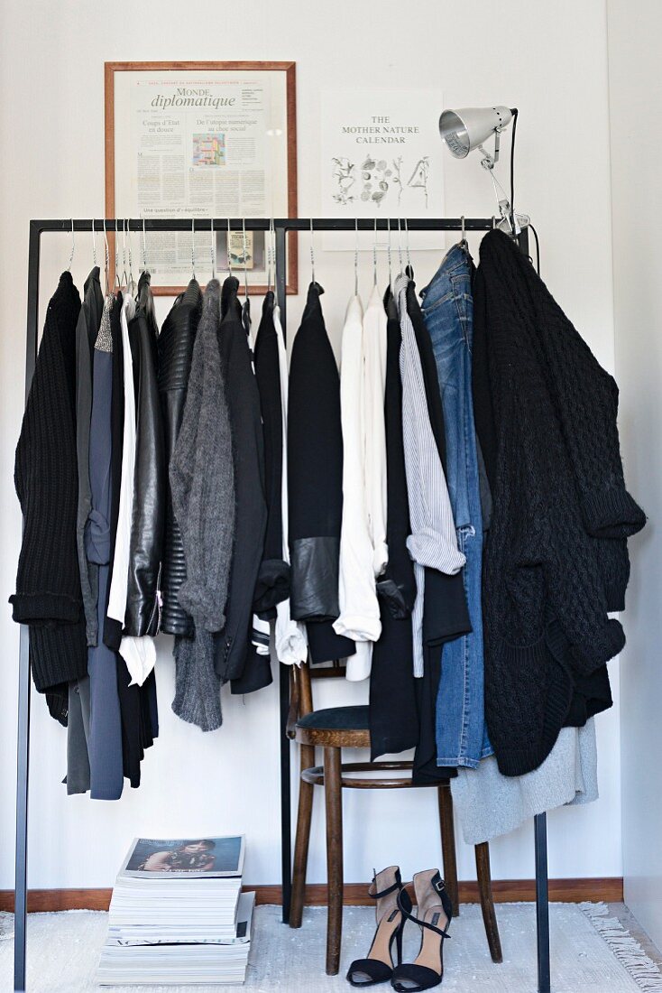 Woman's clothing hung on minimalist metal clothes rail above blac high heels in corner