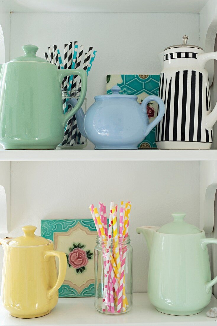 Collection of teapots and coffee pots and colourful drinking straws on white shelves