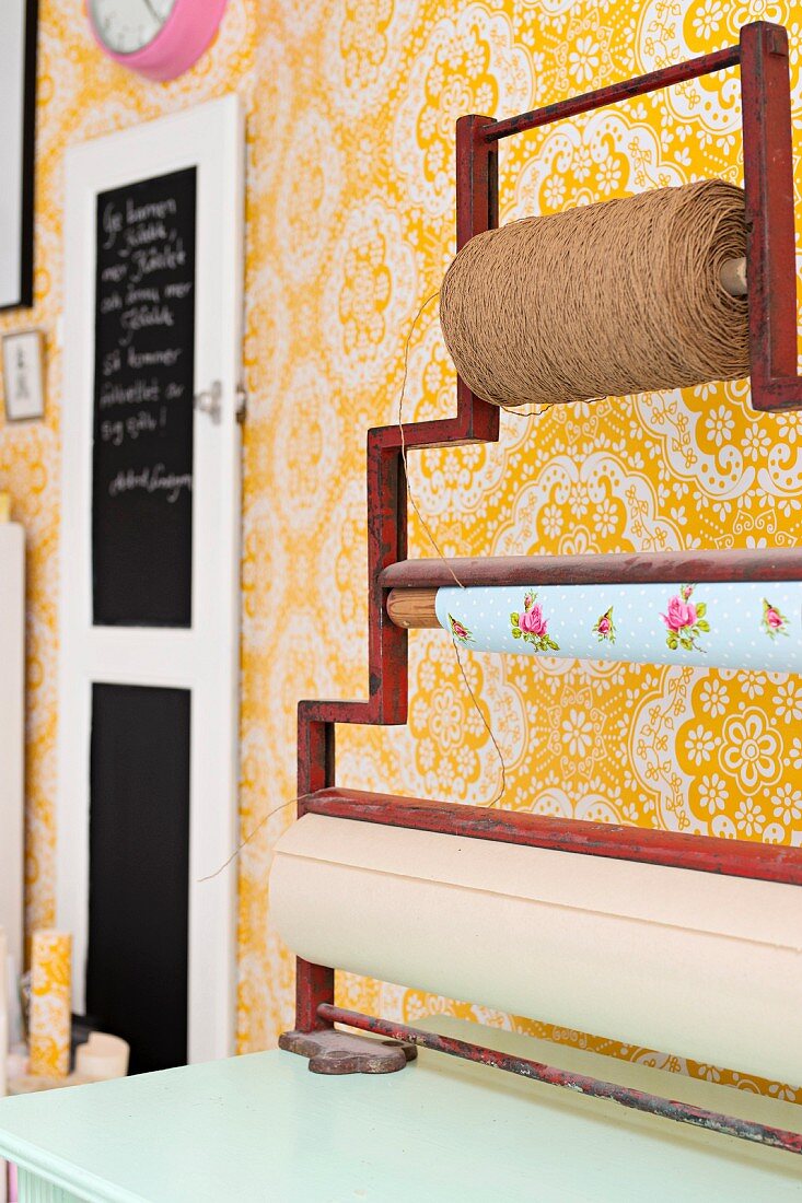 Wrapping table with string, wrapping paper and brown paper rolls on vintage metal frame against yellow and white floral wallpaper