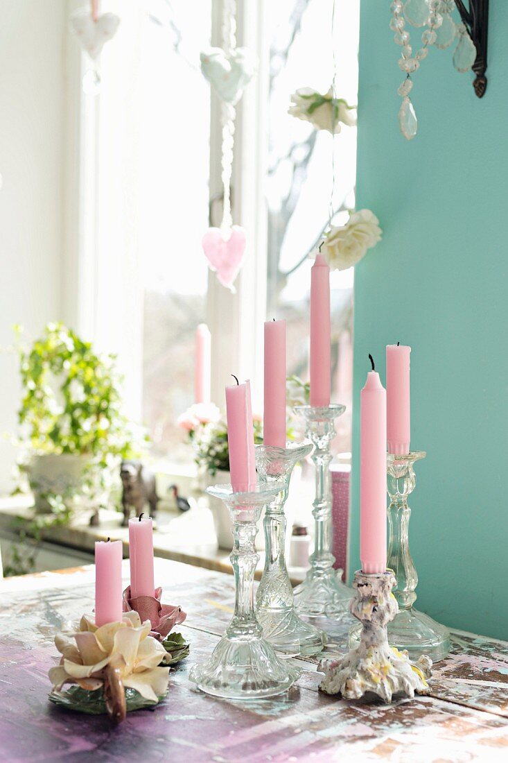 Pink candles in romantic candlesticks on table in front of window