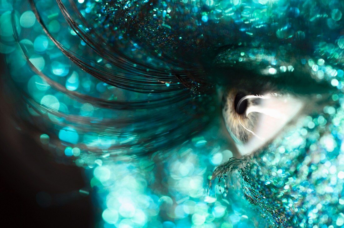 A woman's eye with very long, artificial lashes and glitter on her face
